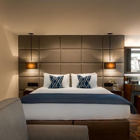 Montcalm Chilworth Townhouse, Paddington Hotel Londres Exterior foto The photo shows a modern hotel room featuring a neatly made bed with two decorative pillows at the headboard. The headboard itself is upholstered in a grid pattern and flanked by wall-mounted lamps. There's a small desk area to the side with a mirror