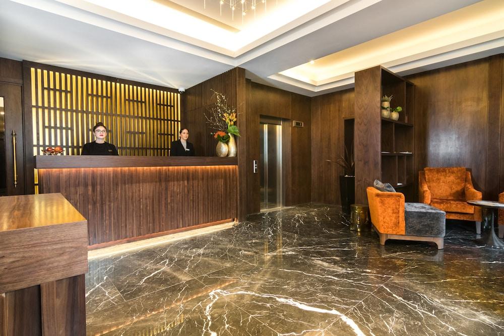 Montcalm Chilworth Townhouse, Paddington Hotel Londres Exterior foto The photo depicts a modern hotel lobby. In the foreground, there is a reception desk made of dark wood, behind which two staff members are standing. The walls are adorned with a wooden panel design and there are decorative plants and flowers on the d