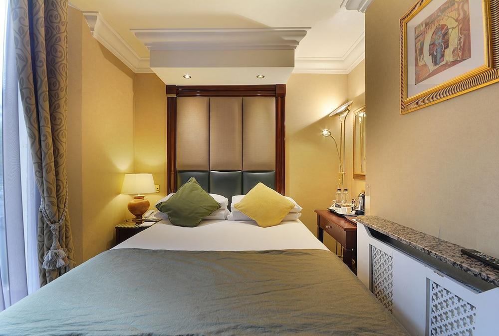 Montcalm Chilworth Townhouse, Paddington Hotel Londres Exterior foto The photo shows a cozy hotel room with a warm color palette. It features a large bed with green and yellow pillows. On one side of the bed, there is a bedside lamp and a small table. Opposite the bed, there is a dresser with a granite top, and a fram