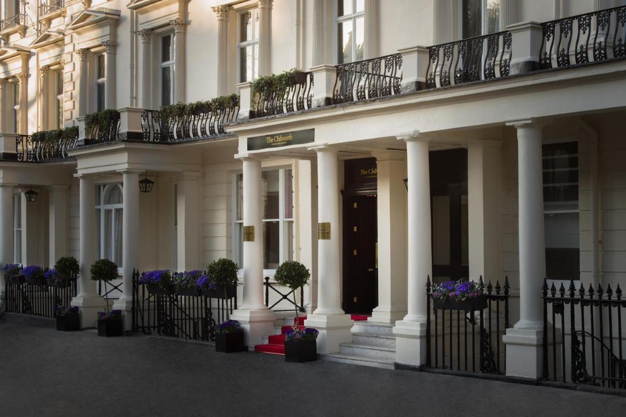 Montcalm Chilworth Townhouse, Paddington Hotel Londres Exterior foto The photo shows an elegant building entrance with classic architectural features. It has several tall, white columns supporting a balcony adorned with ornamental railings. The entrance is flanked by decorative planters with flowers. A set of steps le