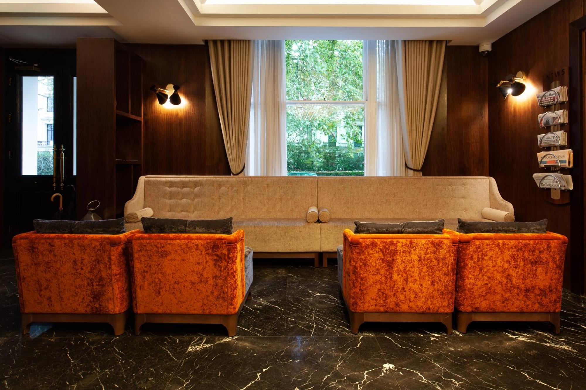 Montcalm Chilworth Townhouse, Paddington Hotel Londres Exterior foto The photo shows a stylish interior space, likely a lounge or sitting area. It features a long, light-colored sofa against a wall with large windows that allow natural light to enter. On either side of the sofa, there are two orange, plush armchairs. 