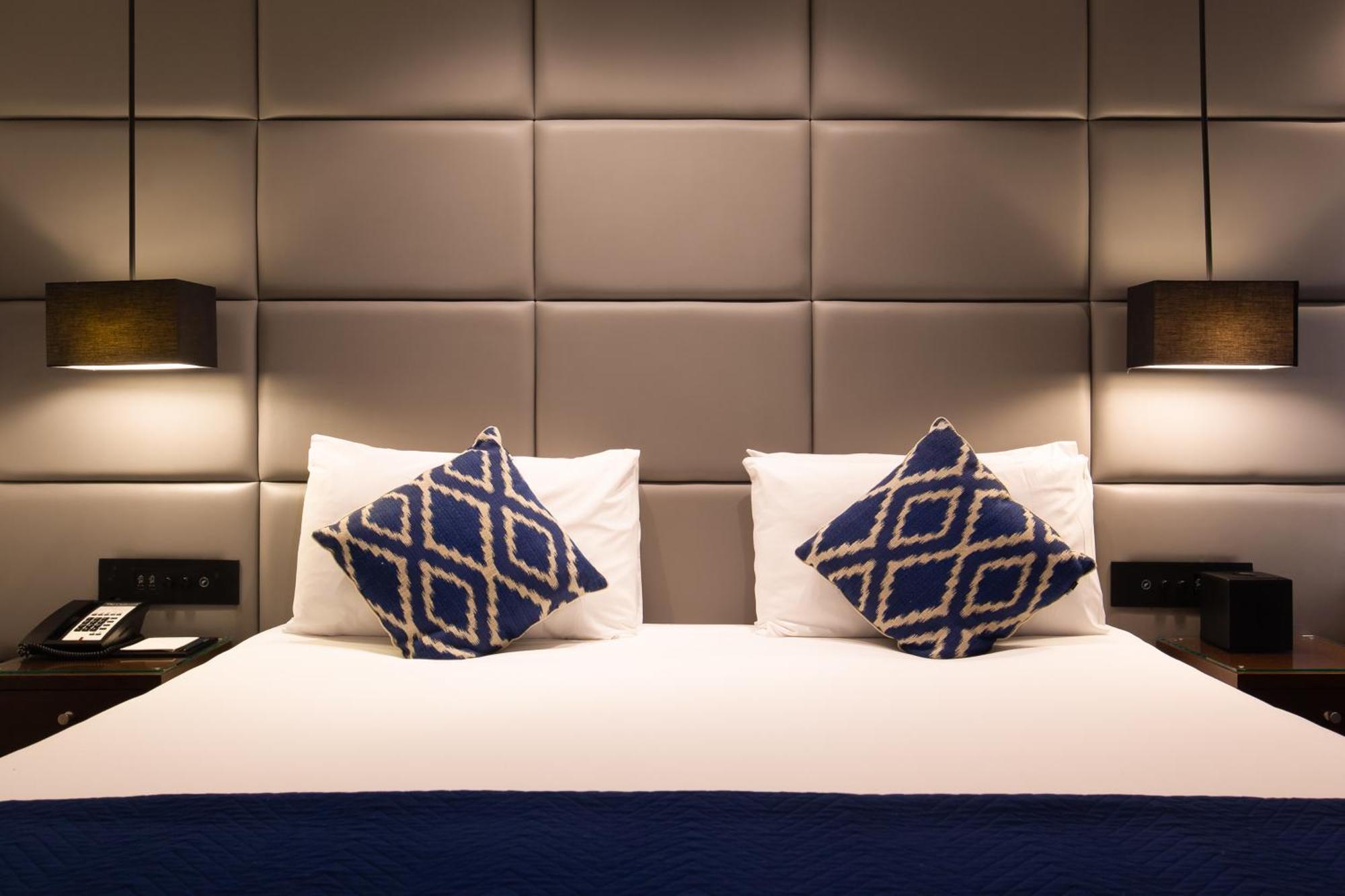 Montcalm Chilworth Townhouse, Paddington Hotel Londres Exterior foto The photo shows a well-designed hotel room with a neatly made bed. The bed has a white duvet and two decorative pillows with a blue geometric pattern. The headboard is upholstered and features a grid-like design in neutral tones. On either side of th