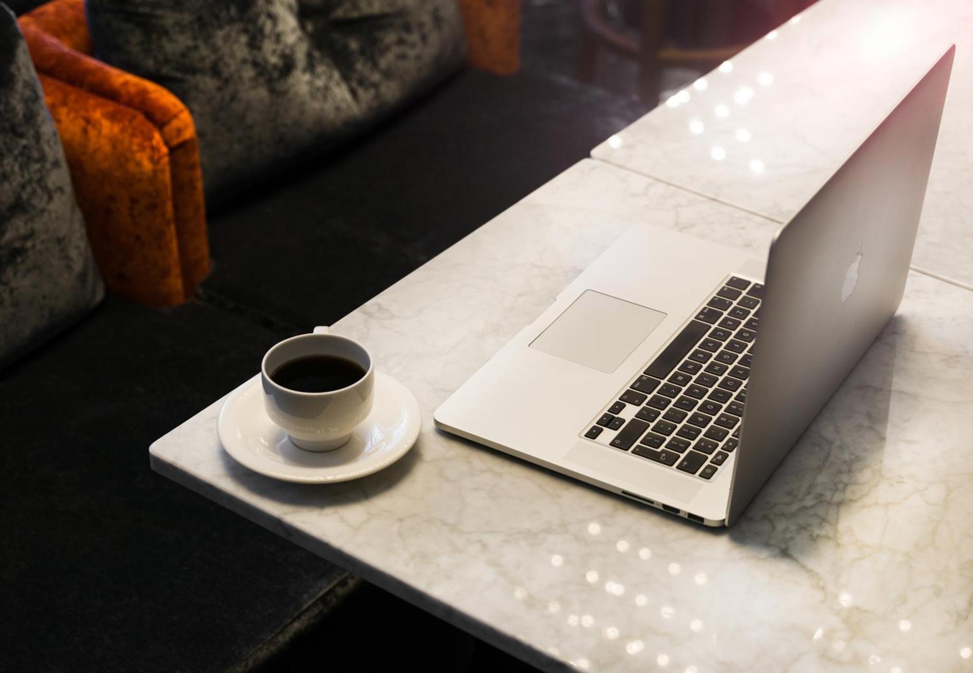 Montcalm Chilworth Townhouse, Paddington Hotel Londres Exterior foto The photo shows a marble table with a laptop positioned on one side. Next to the laptop, there is a small cup of black coffee placed on a saucer. The background features a cozy seating area, with some upholstered chairs that have vibrant orange and d