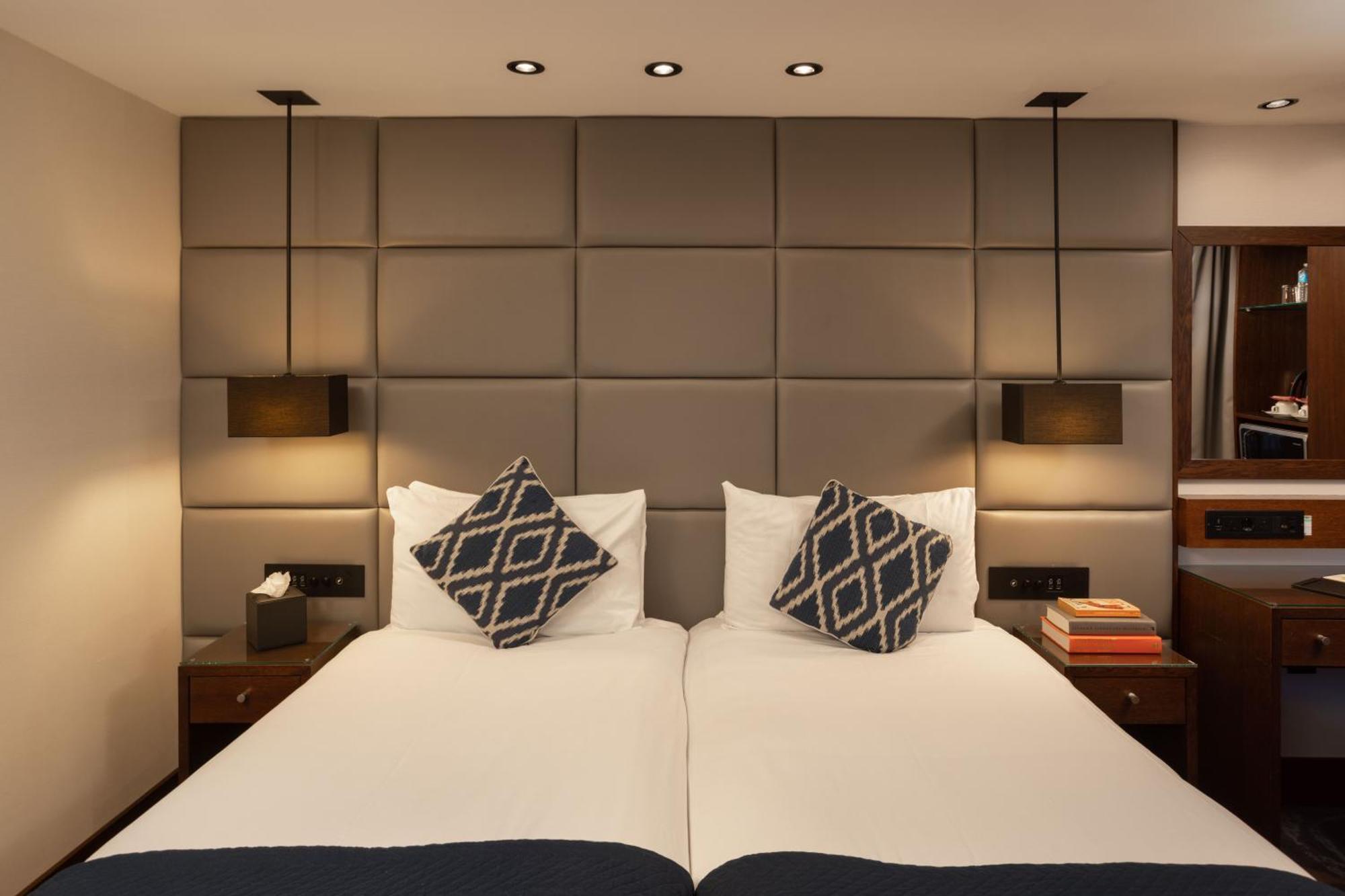 Montcalm Chilworth Townhouse, Paddington Hotel Londres Exterior foto The photo shows a modern bedroom setup with two separate beds positioned next to each other. Each bed has white bedding, and there are decorative pillows with geometric patterns on top. The headboard is designed with a grid of padded squares in a neu