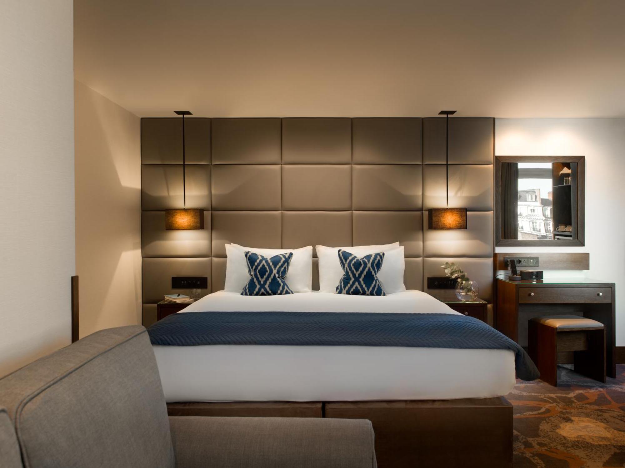 Montcalm Chilworth Townhouse, Paddington Hotel Londres Exterior foto The photo shows a modern hotel room featuring a neatly made bed with two decorative pillows at the headboard. The headboard itself is upholstered in a grid pattern and flanked by wall-mounted lamps. There's a small desk area to the side with a mirror