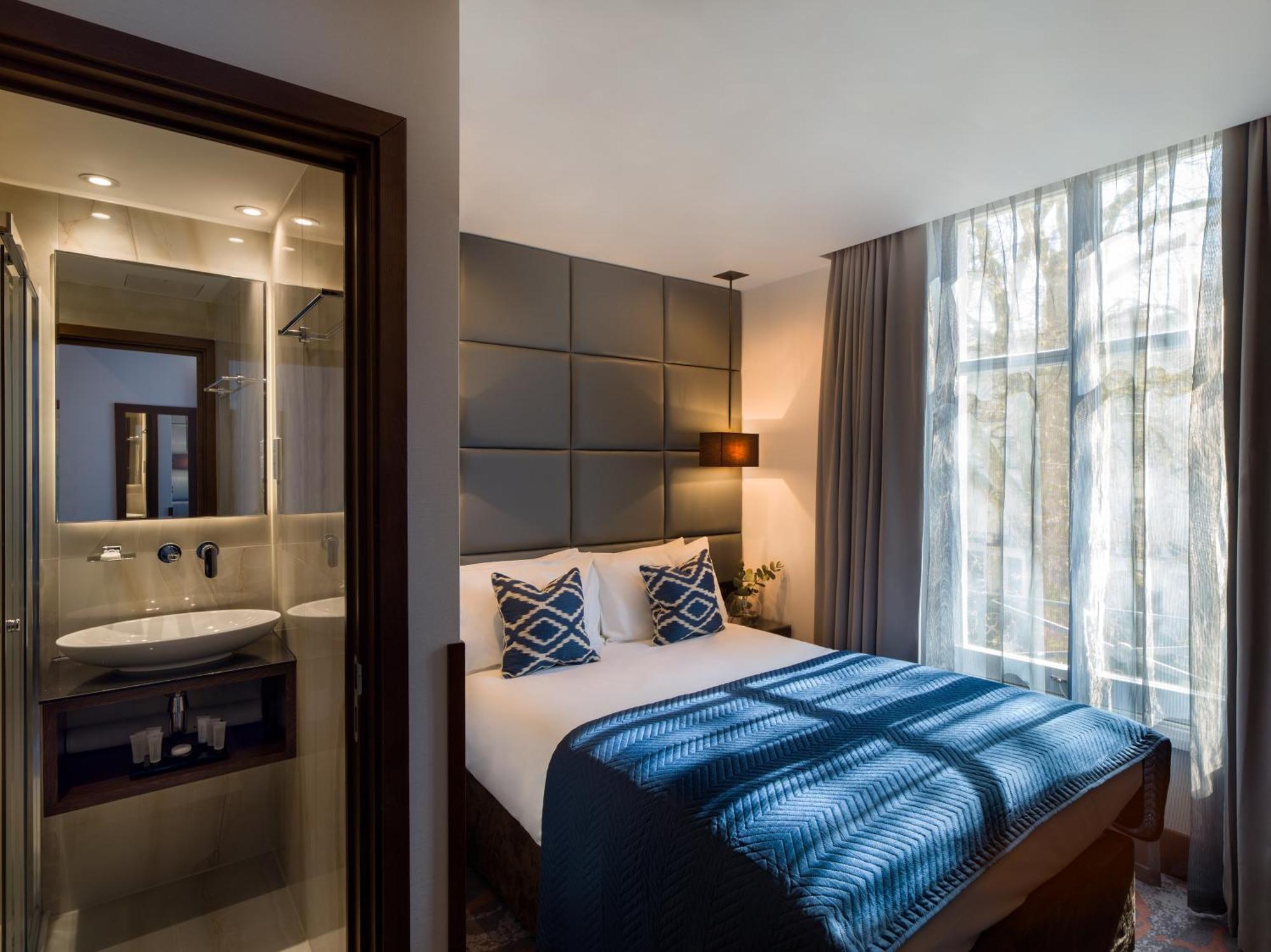 Montcalm Chilworth Townhouse, Paddington Hotel Londres Exterior foto The photo shows a modern hotel bedroom. It features a neatly made bed with blue and white bedding and two decorative pillows. Beside the bed is a lamp, and large windows allow natural light to fill the space, with sheer curtains draping down. On one 