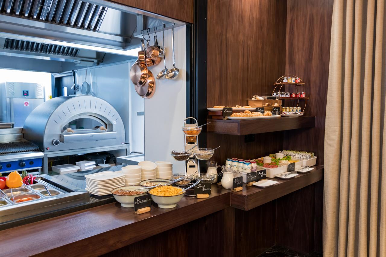 Montcalm Chilworth Townhouse, Paddington Hotel Londres Exterior foto The photo shows a buffet area in a dining setting. There's a wooden counter displaying a variety of food items. On the left side, there are bowls containing different types of food, possibly salads or sides. On a tiered stand, there are desserts or s